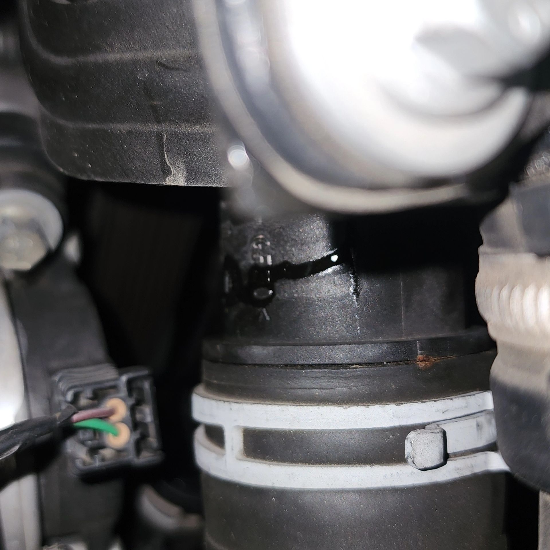 Close-up of black car engine hoses and clamps with a small fluid leak visible.
