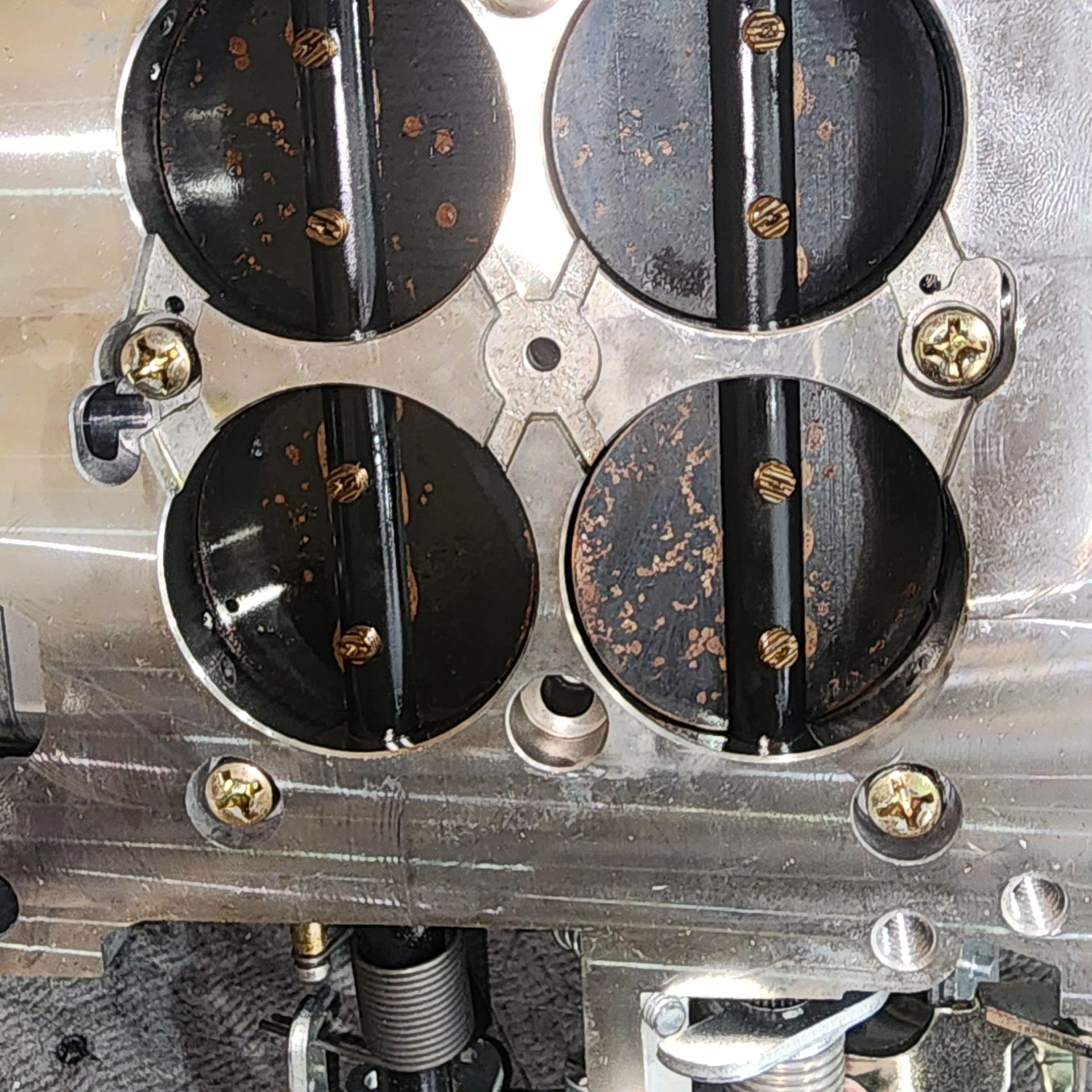 Close-up of a metal mechanical assembly with four black circular plates and rust spots, secured by bolts.