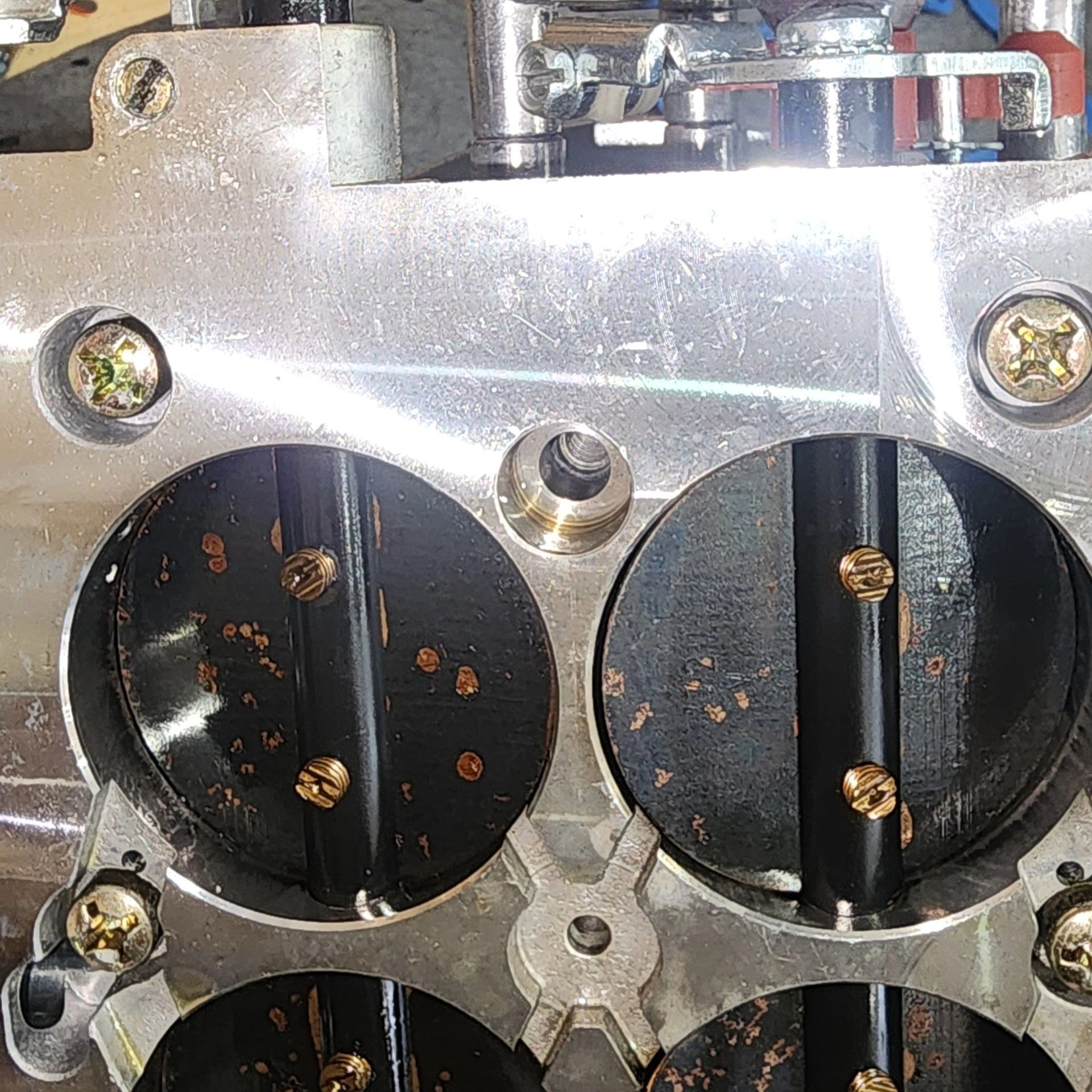 Close-up of a metal throttle body with two black circular valves and brass screws.