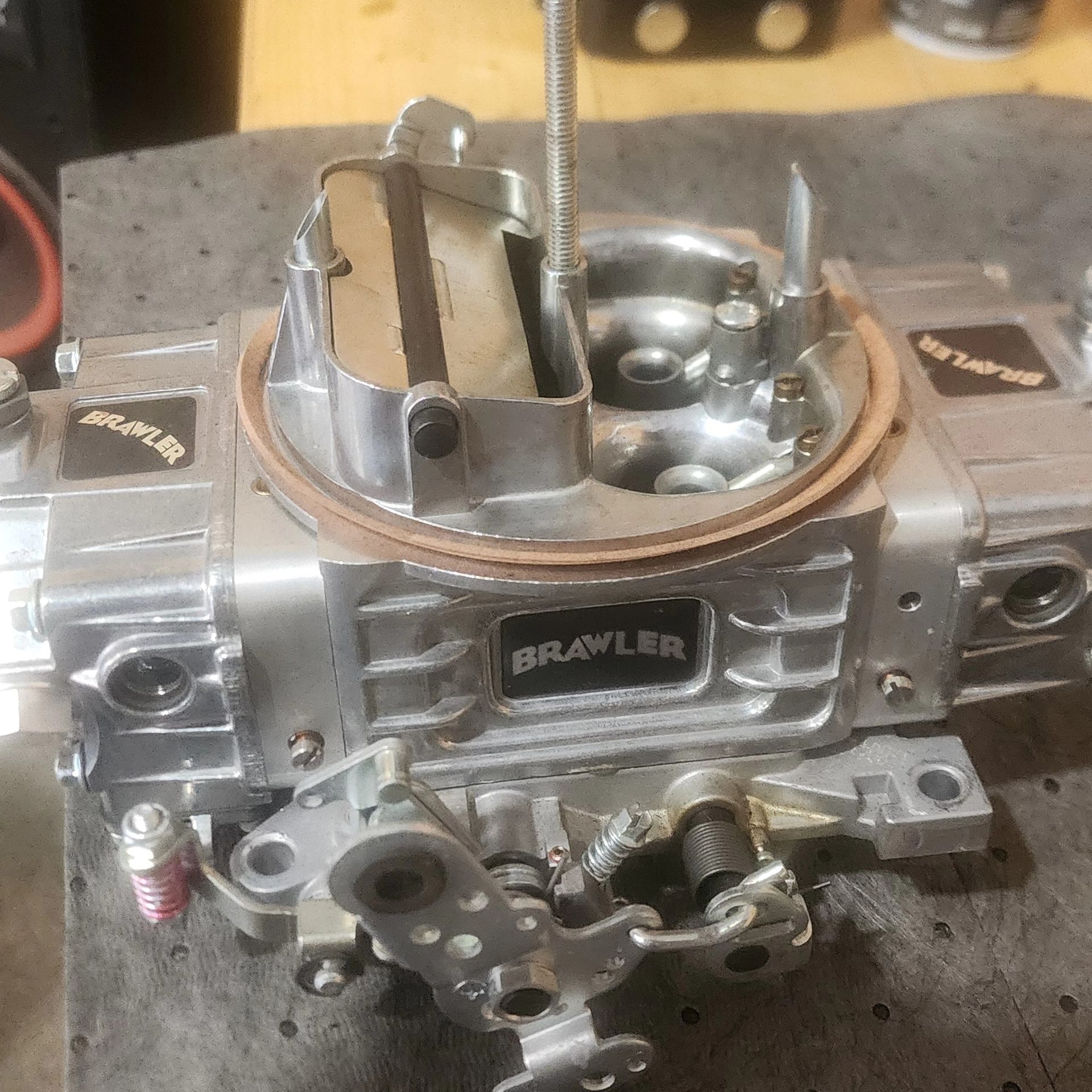 Close-up of a silver Holley carburetor on a workbench, with the throttle bore exposed.
