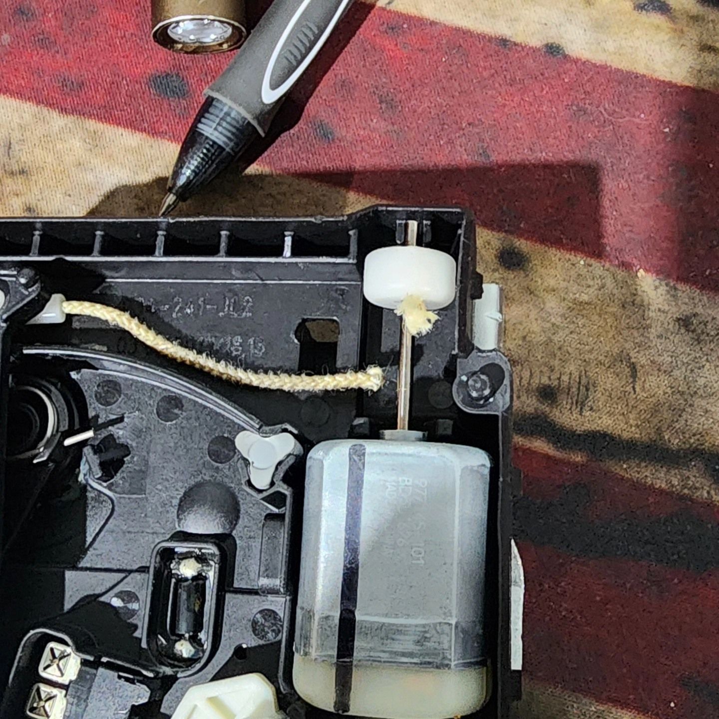 Close-up of a disassembled black motor housing with white gear and silver actuator on a workbench