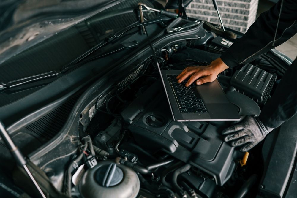 Mechanic using a laptop in a car engine bay during diagnostics