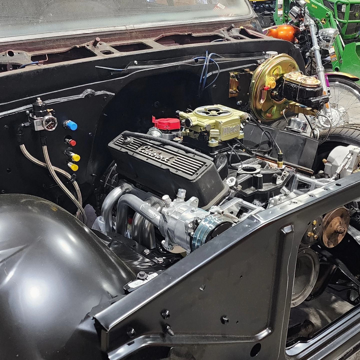 Car engine bay with exposed components, black body panels, and a large gold brake booster.