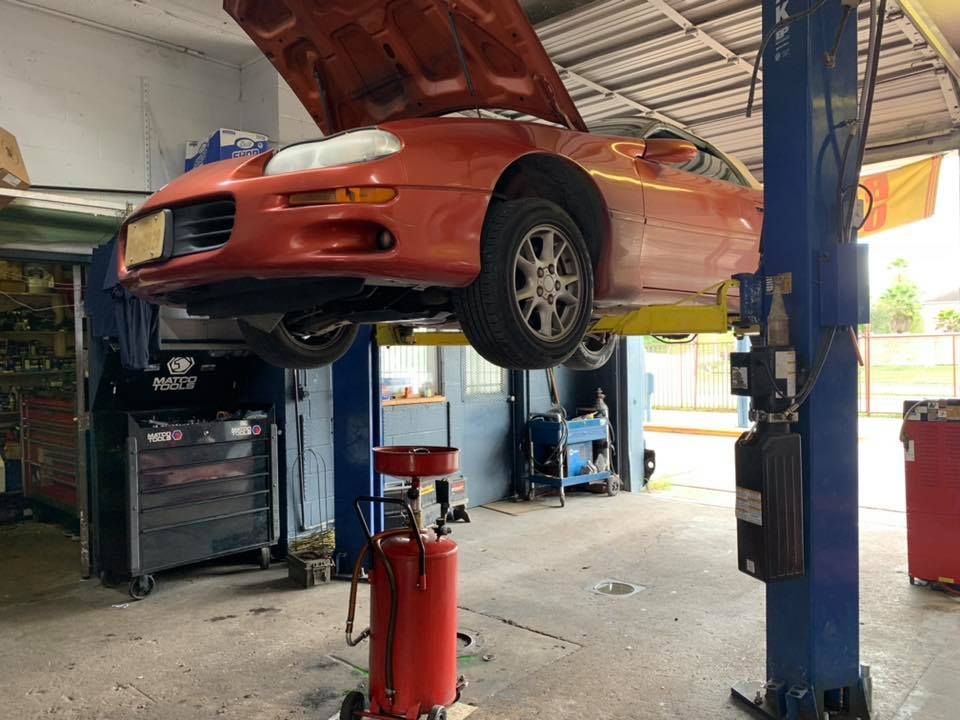 Orange car raised on a lift in a repair shop. The hood is open. | William’s Auto Repair