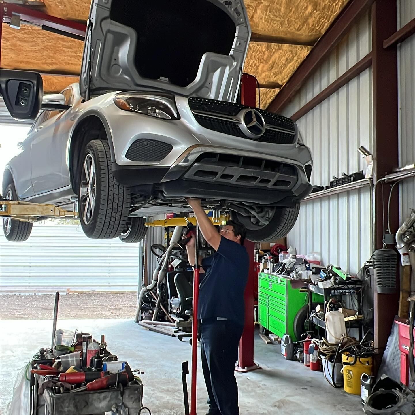 Mechanic working on a silver Mercedes SUV lifted in a garage. | William’s Auto Repair