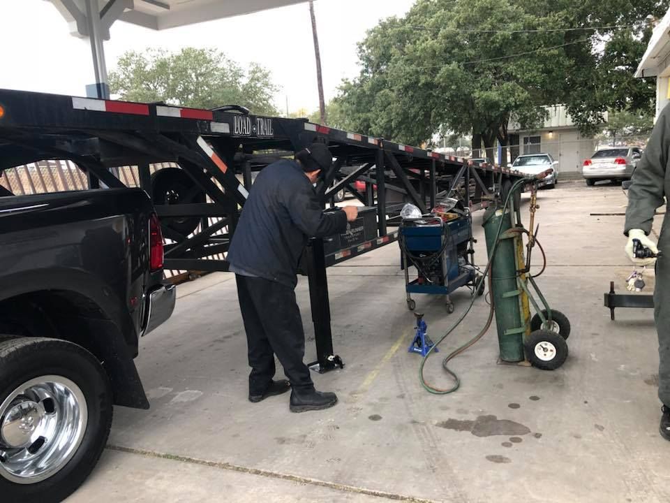 A person works on a car hauler trailer next to a truck. Welding equipment is nearby. | William’s Auto Repair