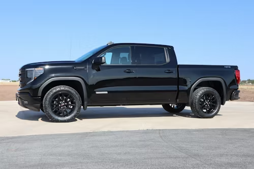 A black GMC Sierra crew cab pickup truck parked on a paved lot under a clear blue sky.