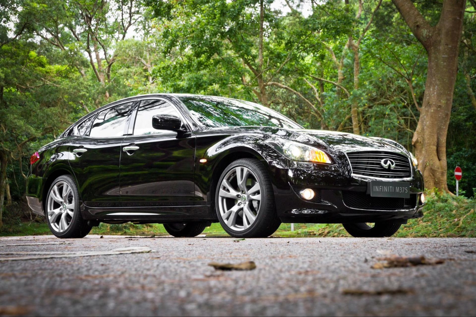 A black car is parked on the side of a road in front of trees.