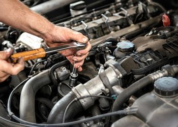 A man is working on a car engine with a wrench.