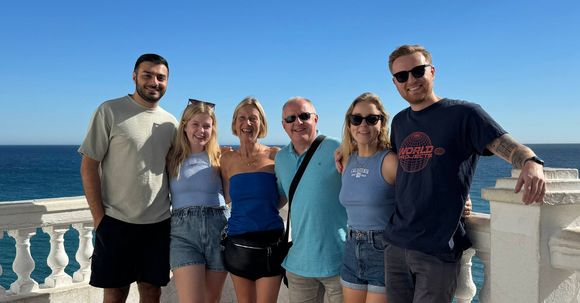 A group of people are posing for a picture on a balcony overlooking the ocean.