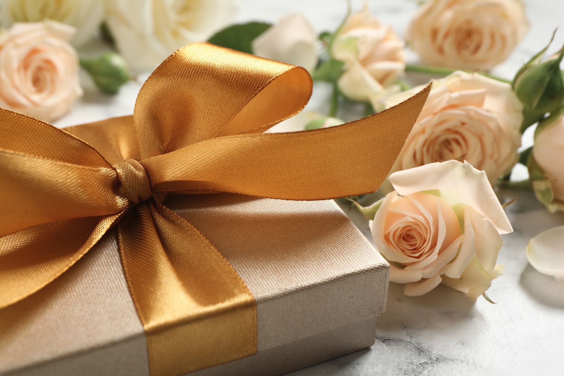 Gift box with a gold ribbon surrounded by cream roses