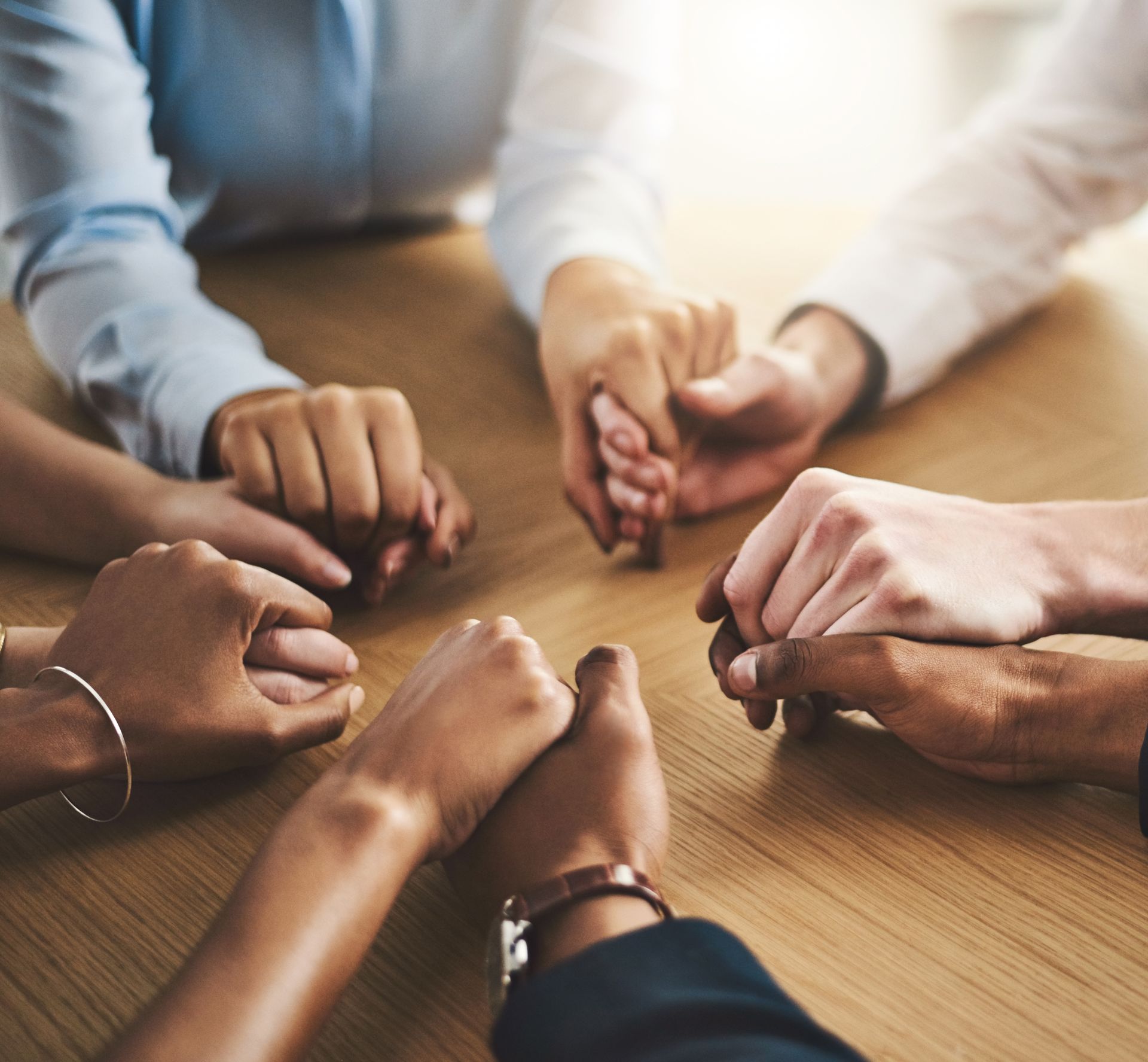 Hands of several people joined in a circle over a wooden table, suggesting teamwork or discussion