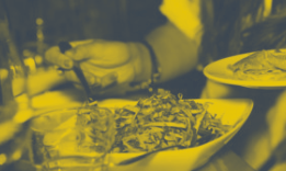 Plates of food being served, with a person's hand reaching over the dishes; yellow-tinted.