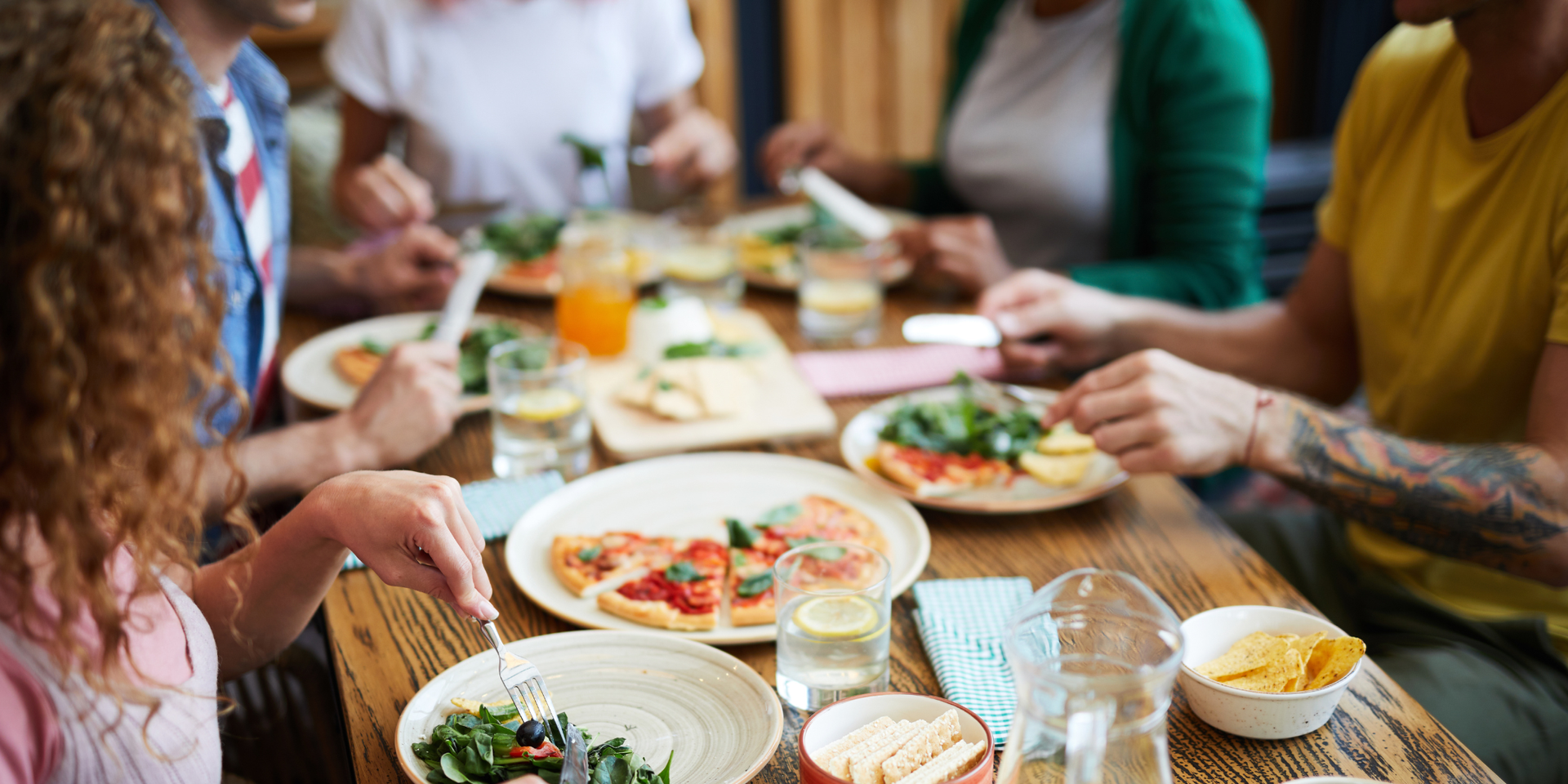 Plates of food being served at a restaurant, hand of server visible. Yellow and blue color grade.