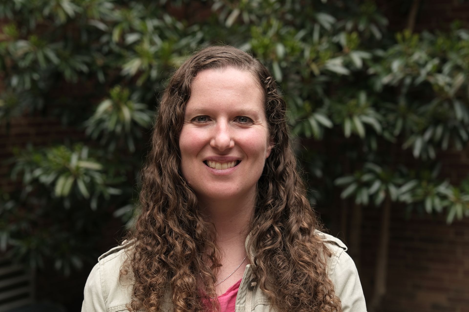 woman with wavy hair smiling at camera in front of greenery