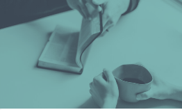 Hands holding a cup and flipping a book on a teal table.