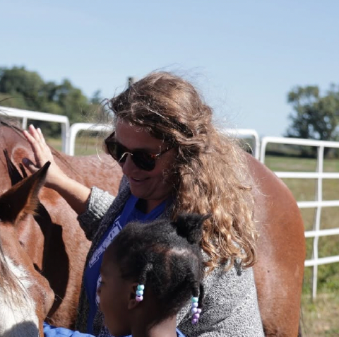 Woman with sunglasses petting a horse with child