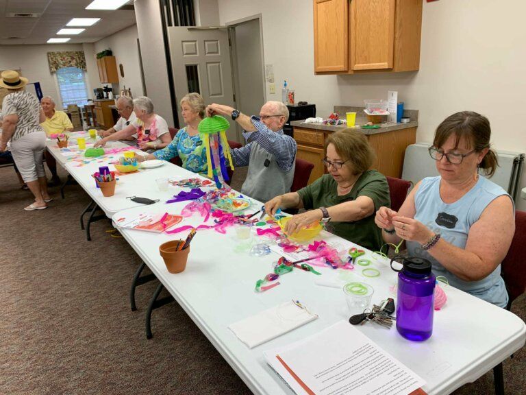 Seniors at a table crafting with colorful materials, in a community center setting.