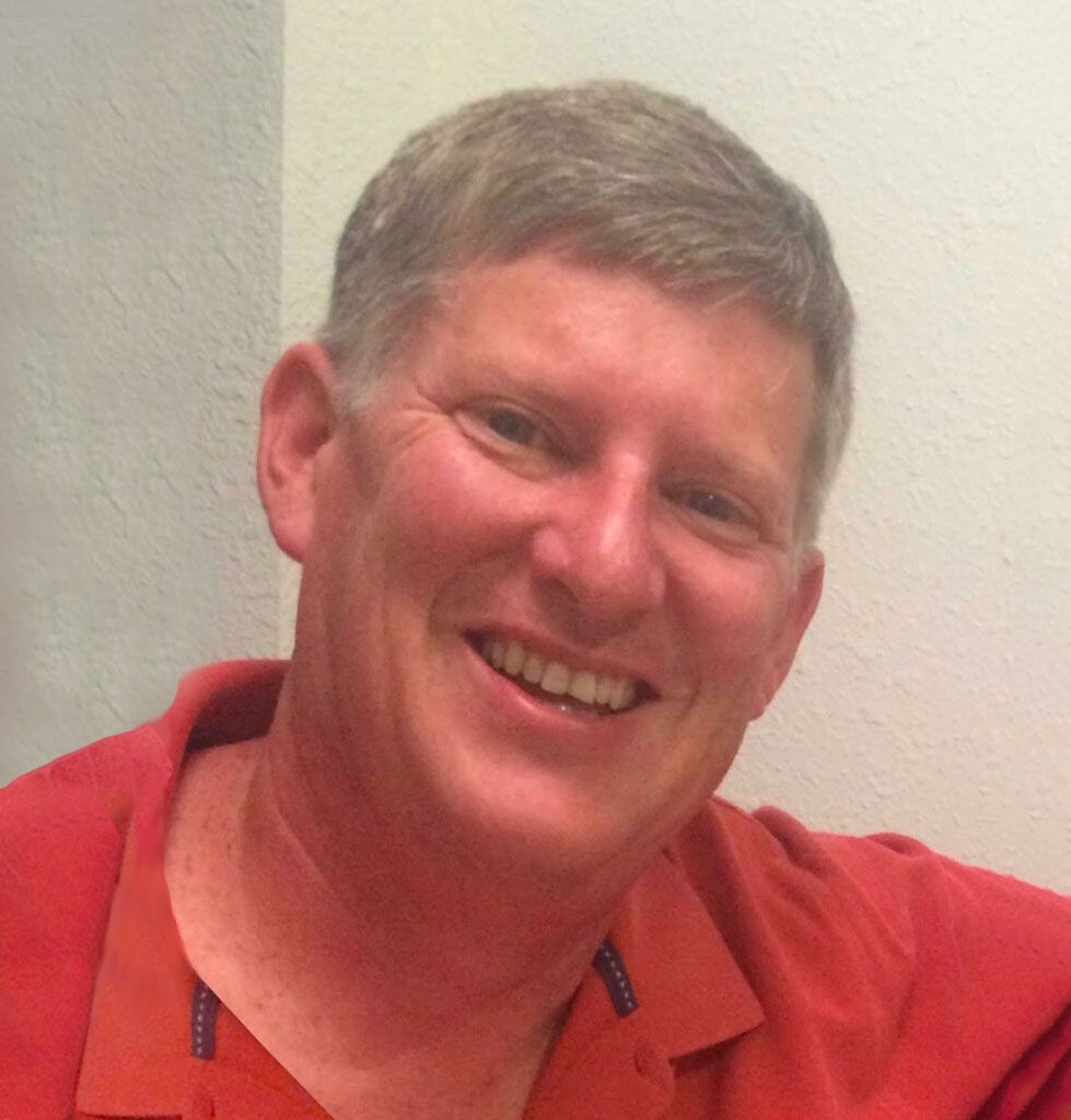 Smiling middle-aged man with short gray hair wearing a red polo shirt.