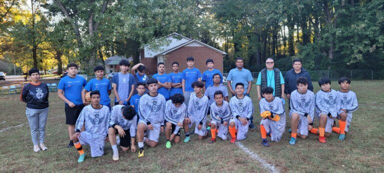 A youth soccer team in blue and gray uniforms kneels and stands on a grassy field.