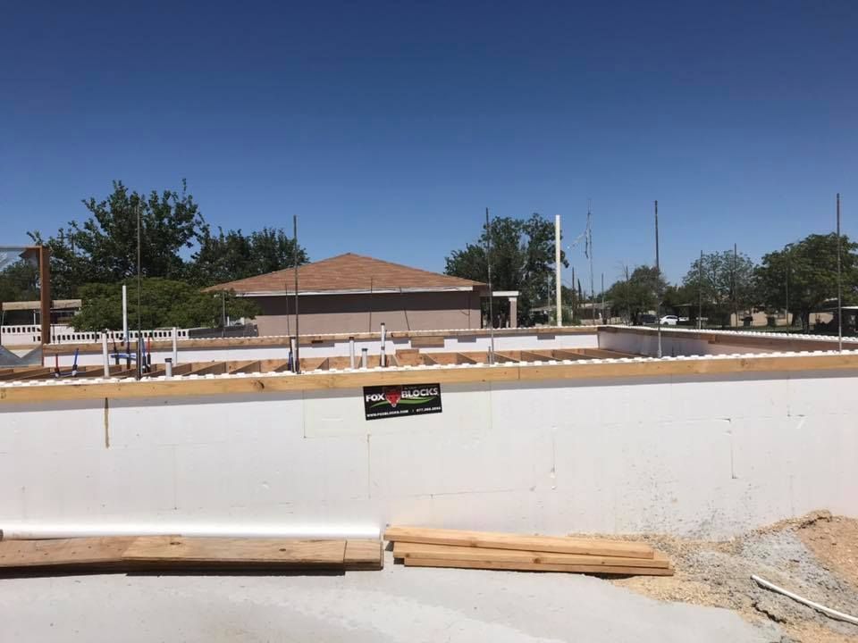 A building under construction with a house in the background.