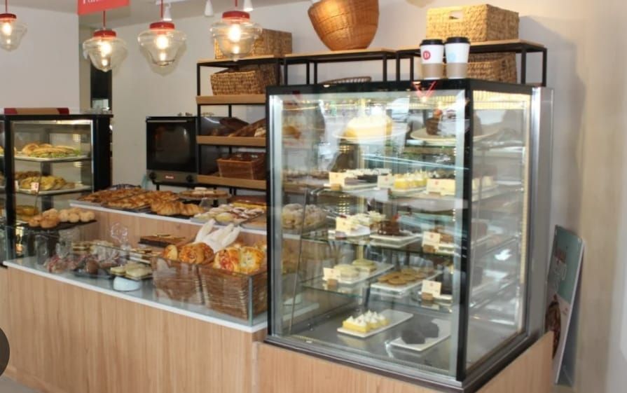 Interior de panadería: vitrinas repletas de pasteles, panes y tartas, con mostrador y estantes de madera clara.