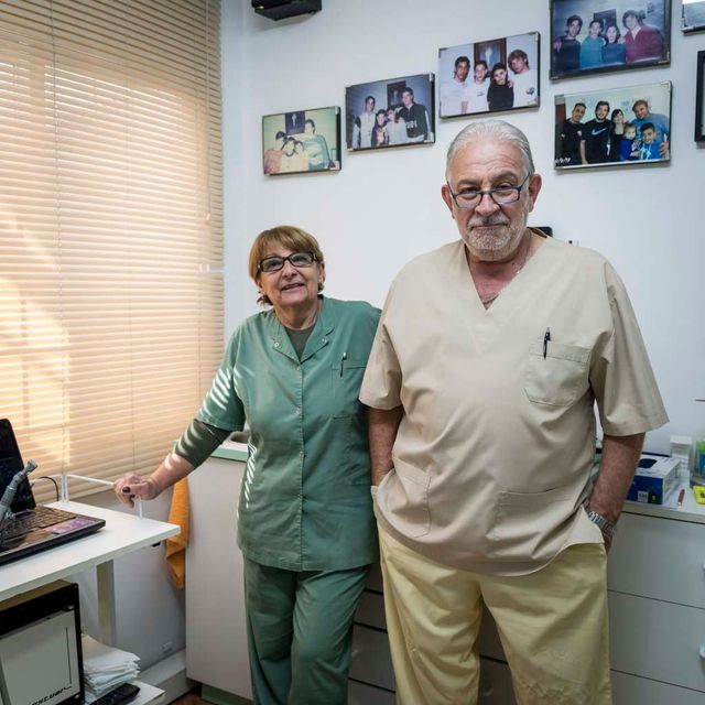 Dos trabajadores sanitarios con uniforme quirúrgico de pie en una oficina luminosa con fotos enmarcadas en la pared.