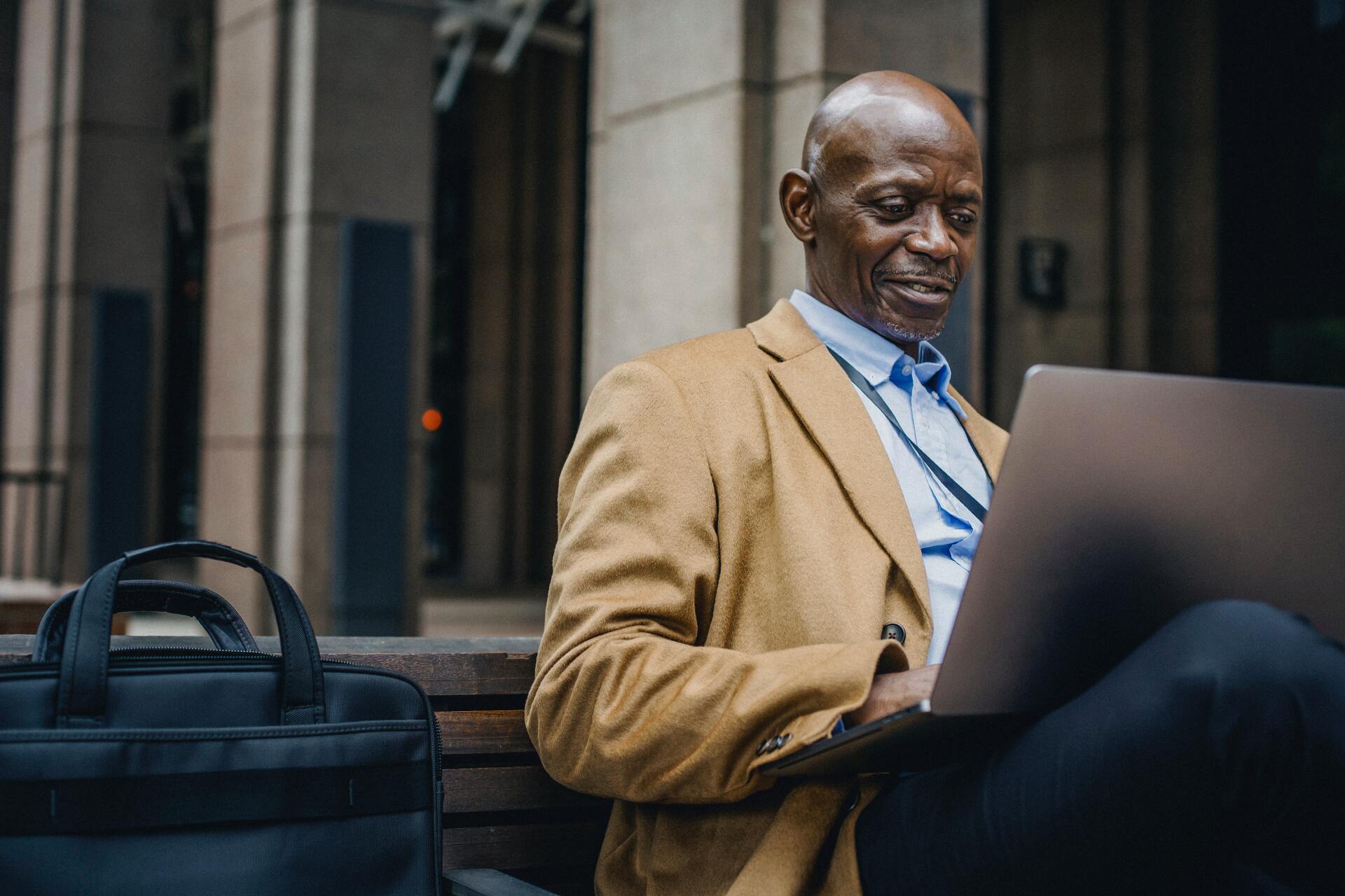 A man in a suit is sitting on a bench using a laptop computer.