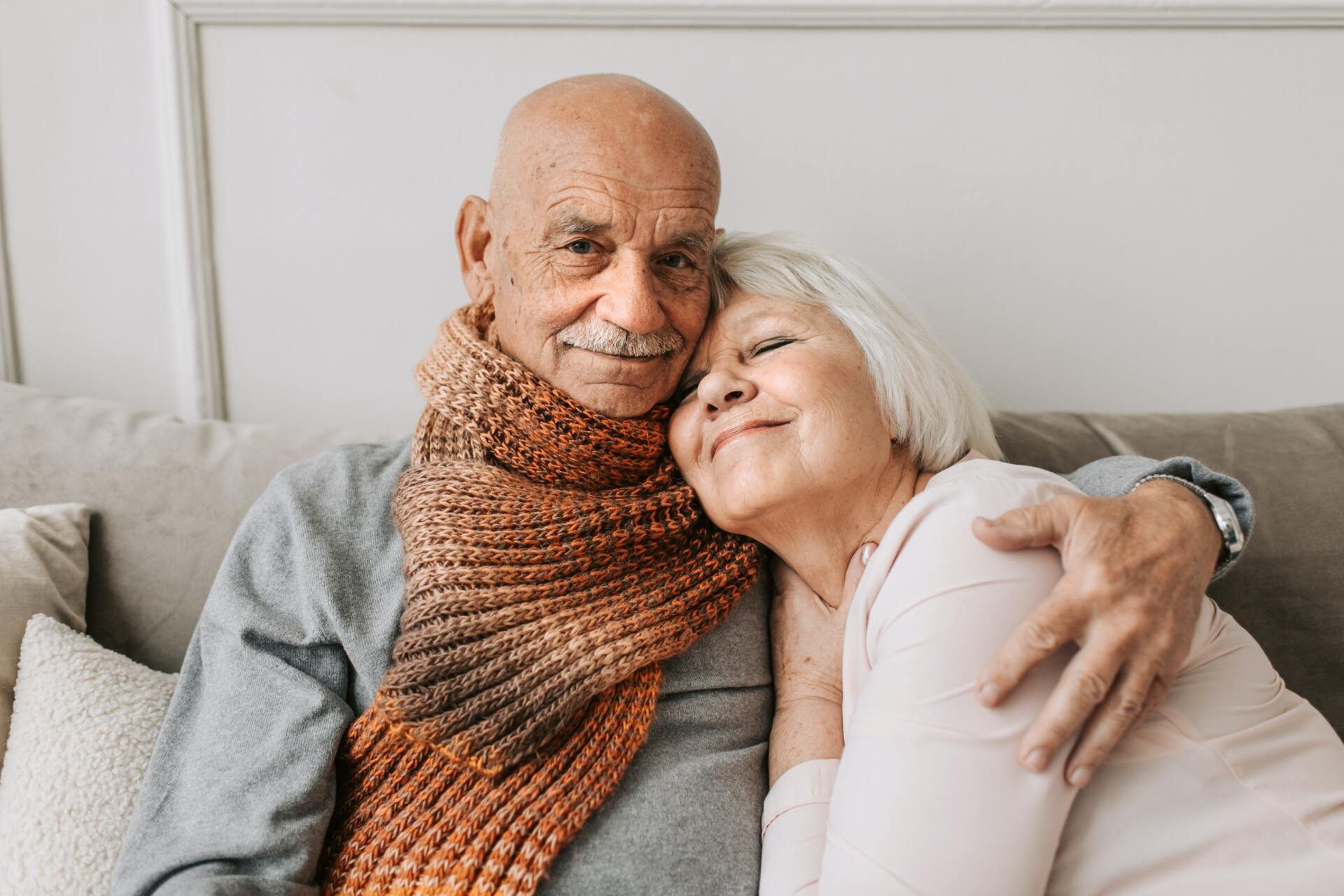 An elderly couple is sitting on a couch hugging each other.