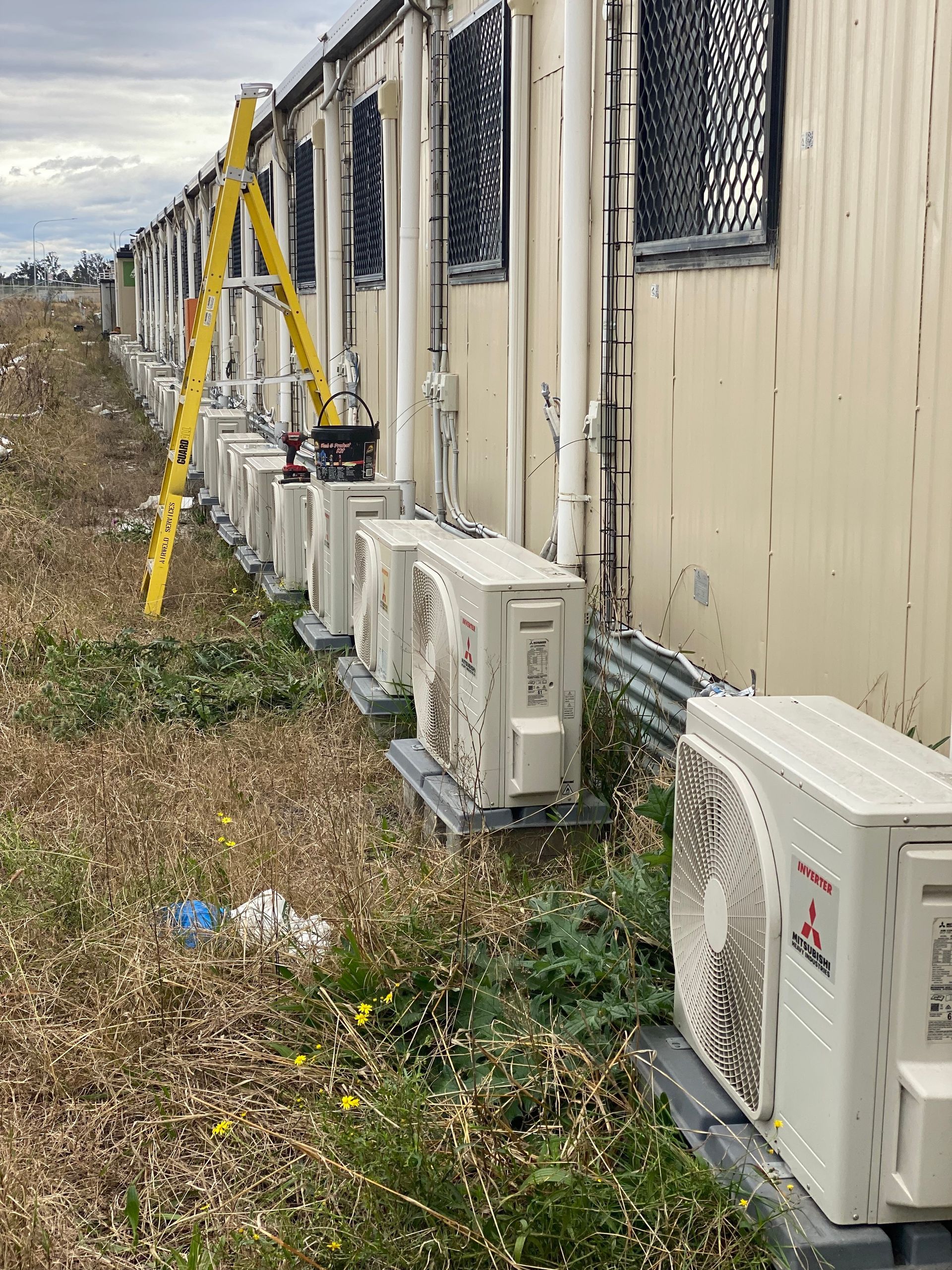 Row of beige portable buildings with multiple air conditioning units. A yellow ladder leans against one. — Airweld Services Pty Ltd in Nowra, NSW