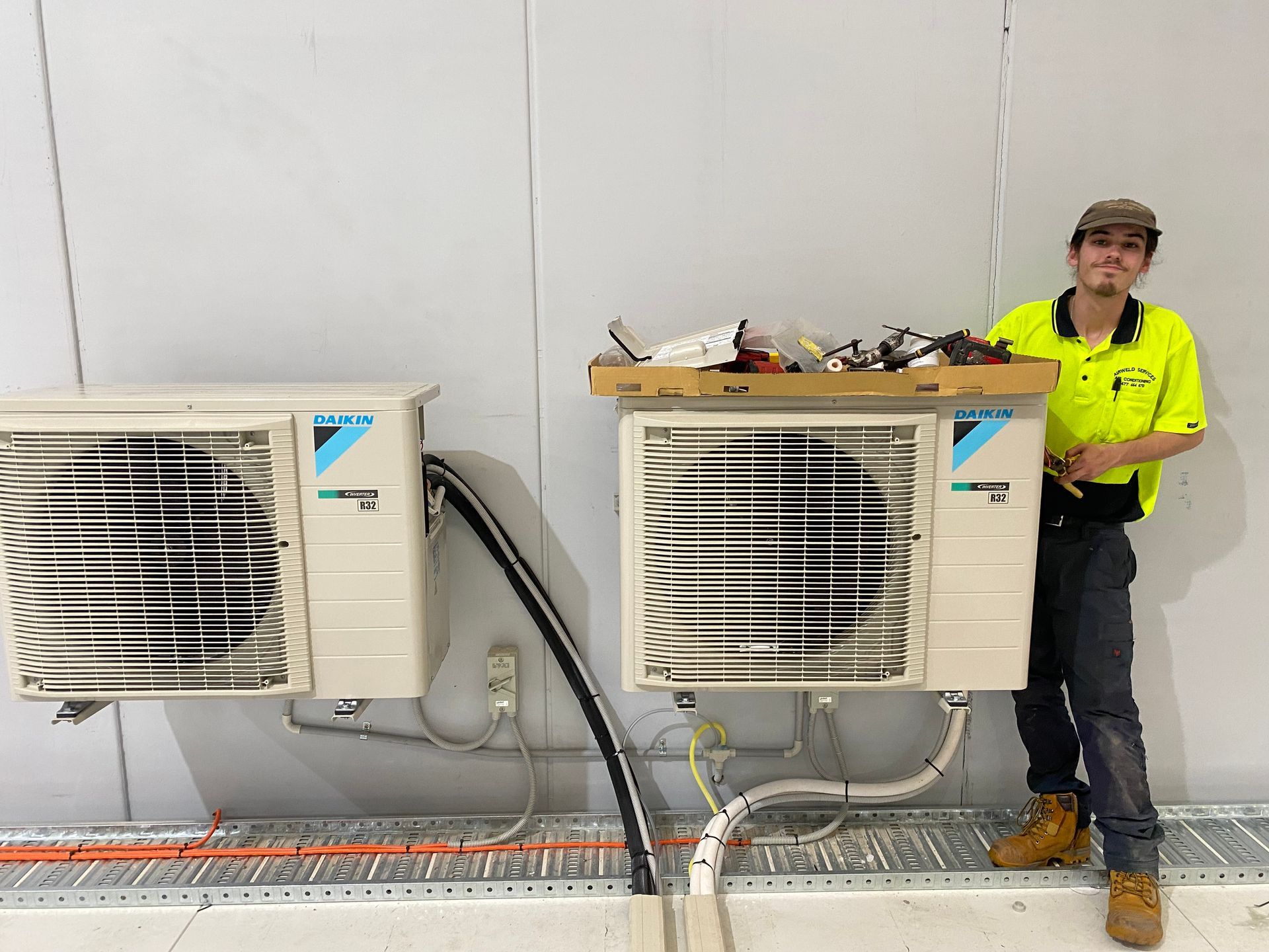 Man in work clothes beside two air conditioning units on a wall. — Airweld Services Pty Ltd in Nowra, NSW