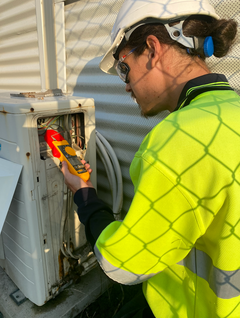 Worker in Neon Jacket Inspecting an Outdoor Electrical Unit With a Tool — Airweld Services Pty Ltd in Shellharbour, NSW