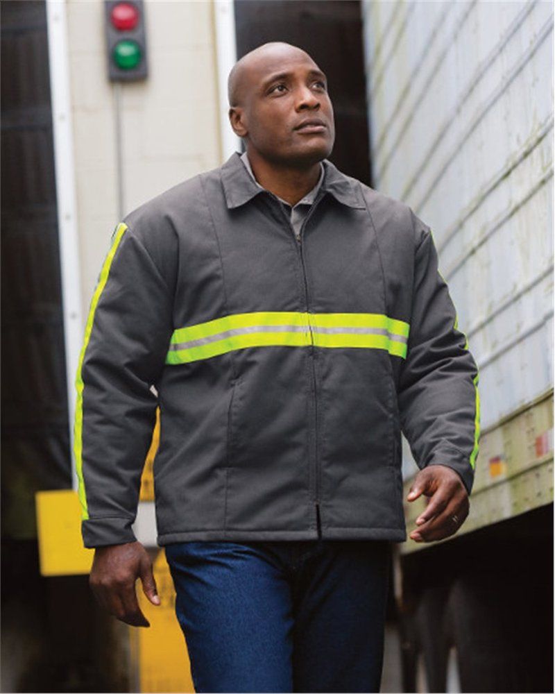 Person in grey work jacket with reflective stripes, standing near a truck.
