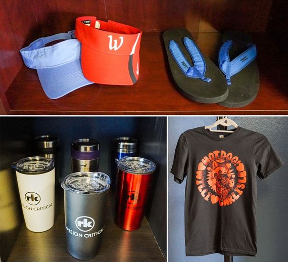 Caps, flip-flops, tumblers, and a t-shirt displaying logo and designs, on shelves.