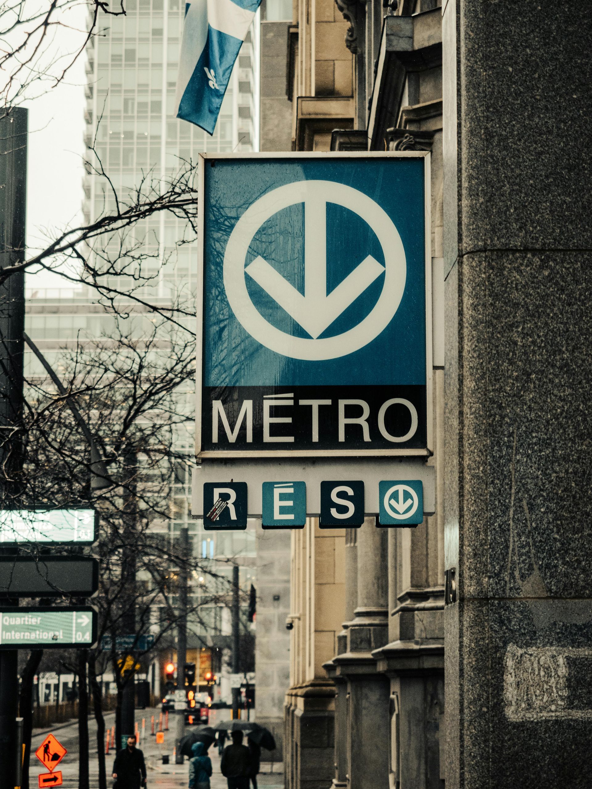 Montreal Metro station sign on a building, with city street and pedestrians.
