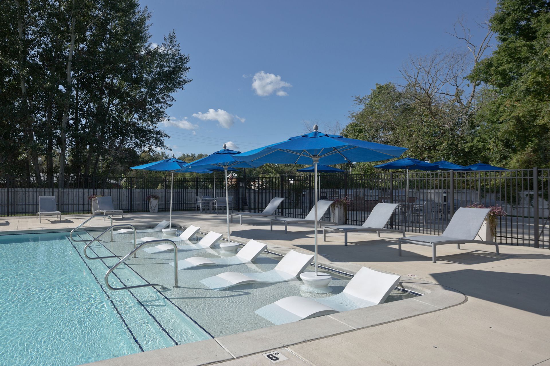 Pool area with chaise lounges, blue umbrellas, and steps into the water on a sunny day.