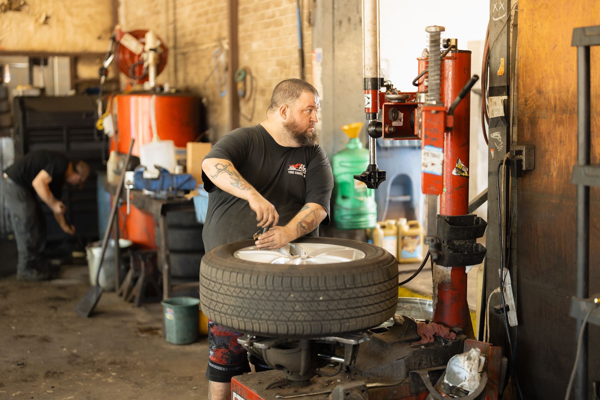 Mechanic working on a tire in an auto repair garage with tools and equipment nearby