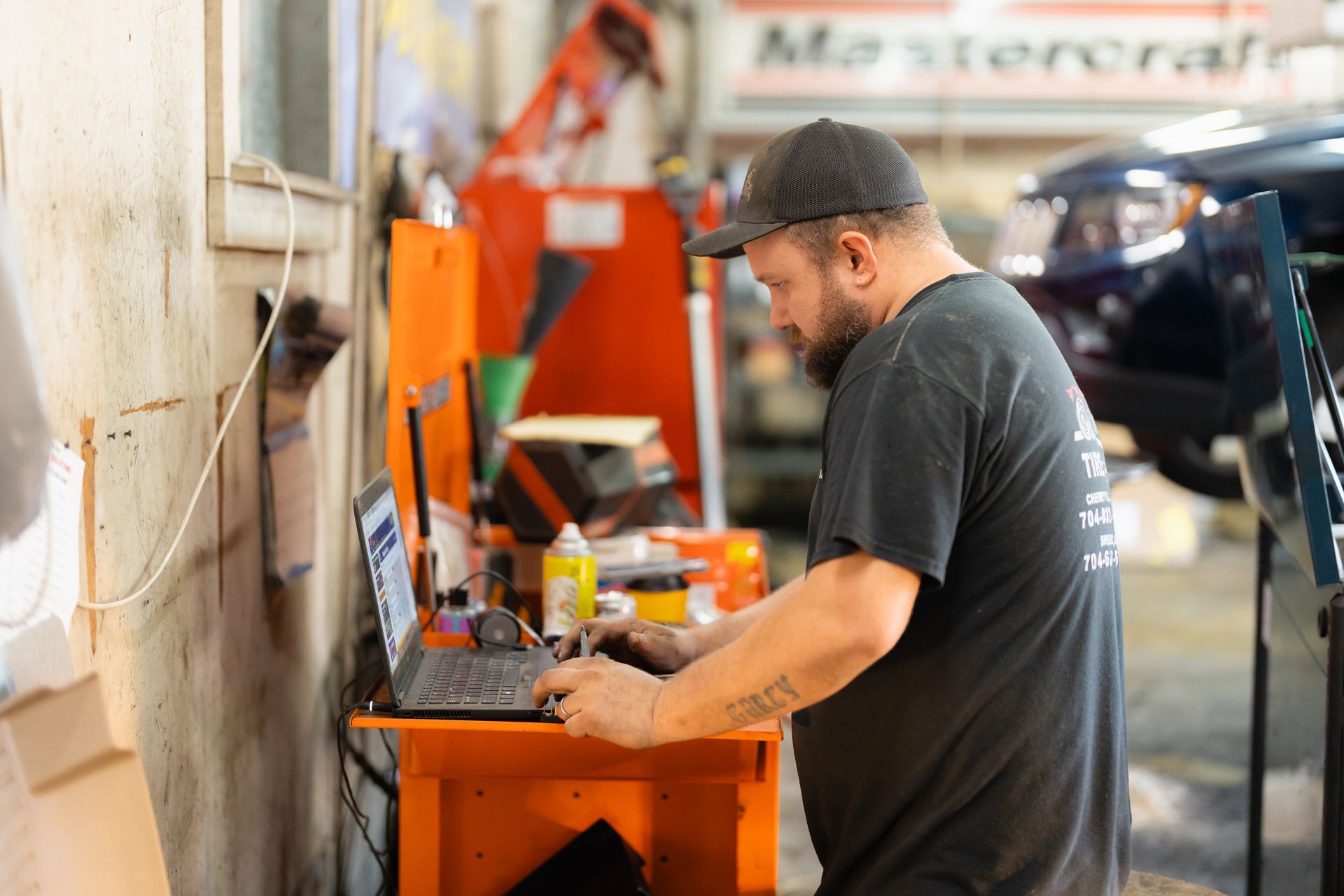 Man working on a laptop at an orange workbench in an auto repair shop