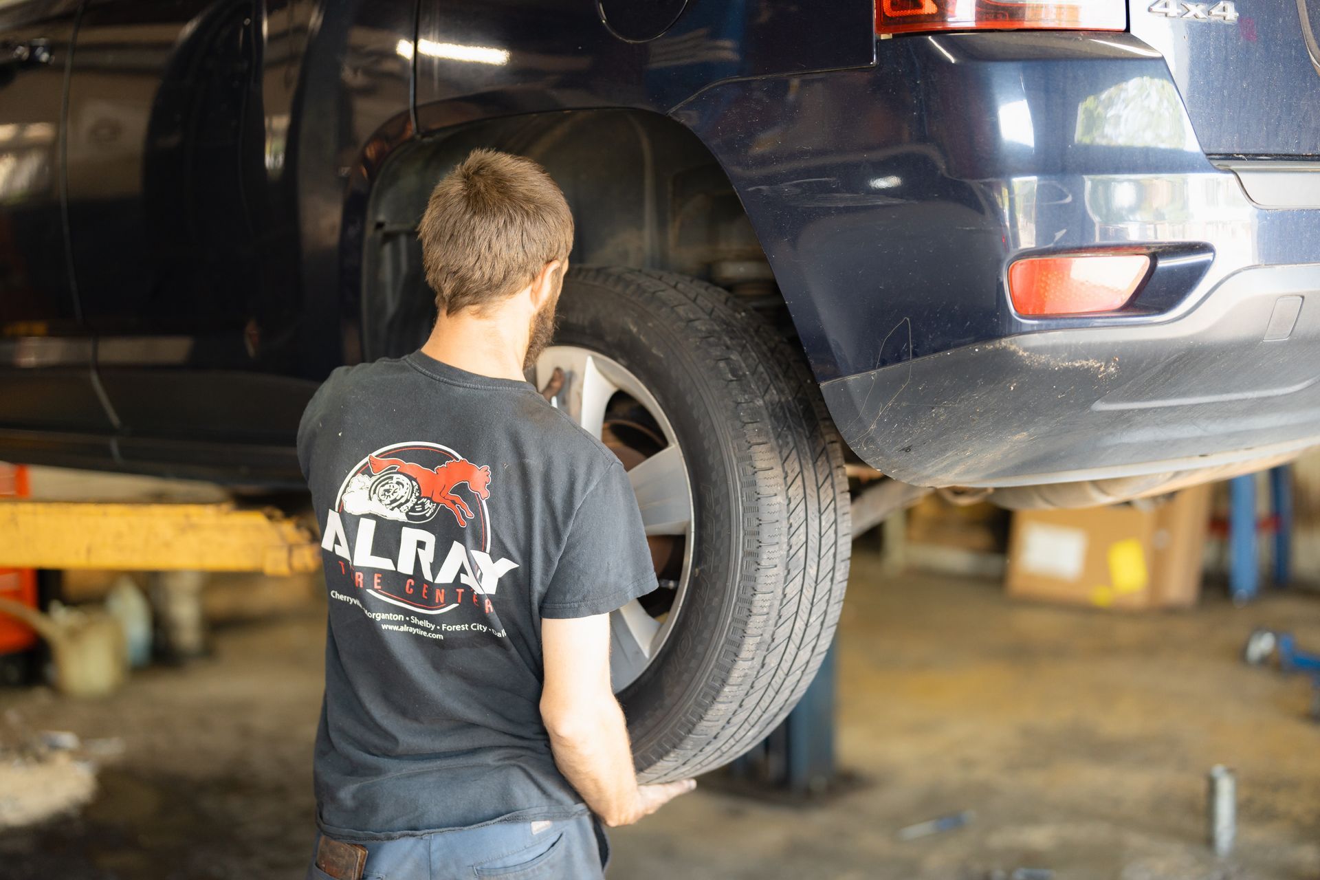 Mechanic inspecting a car’s rear wheel in a garage, with the vehicle raised on a lift.