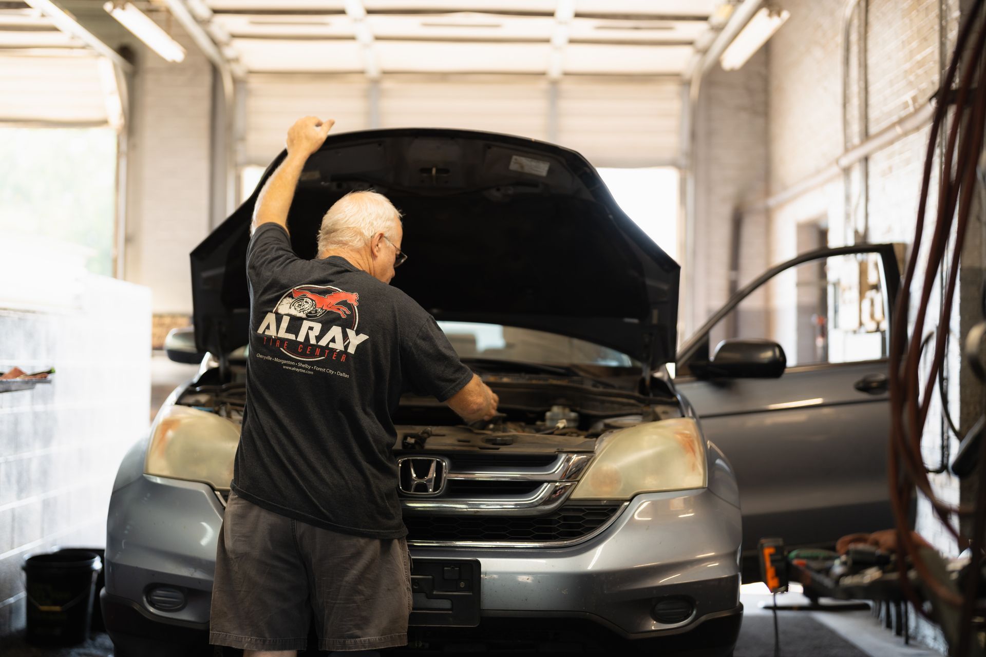 Mechanic working under the hood of a silver Honda in a garage