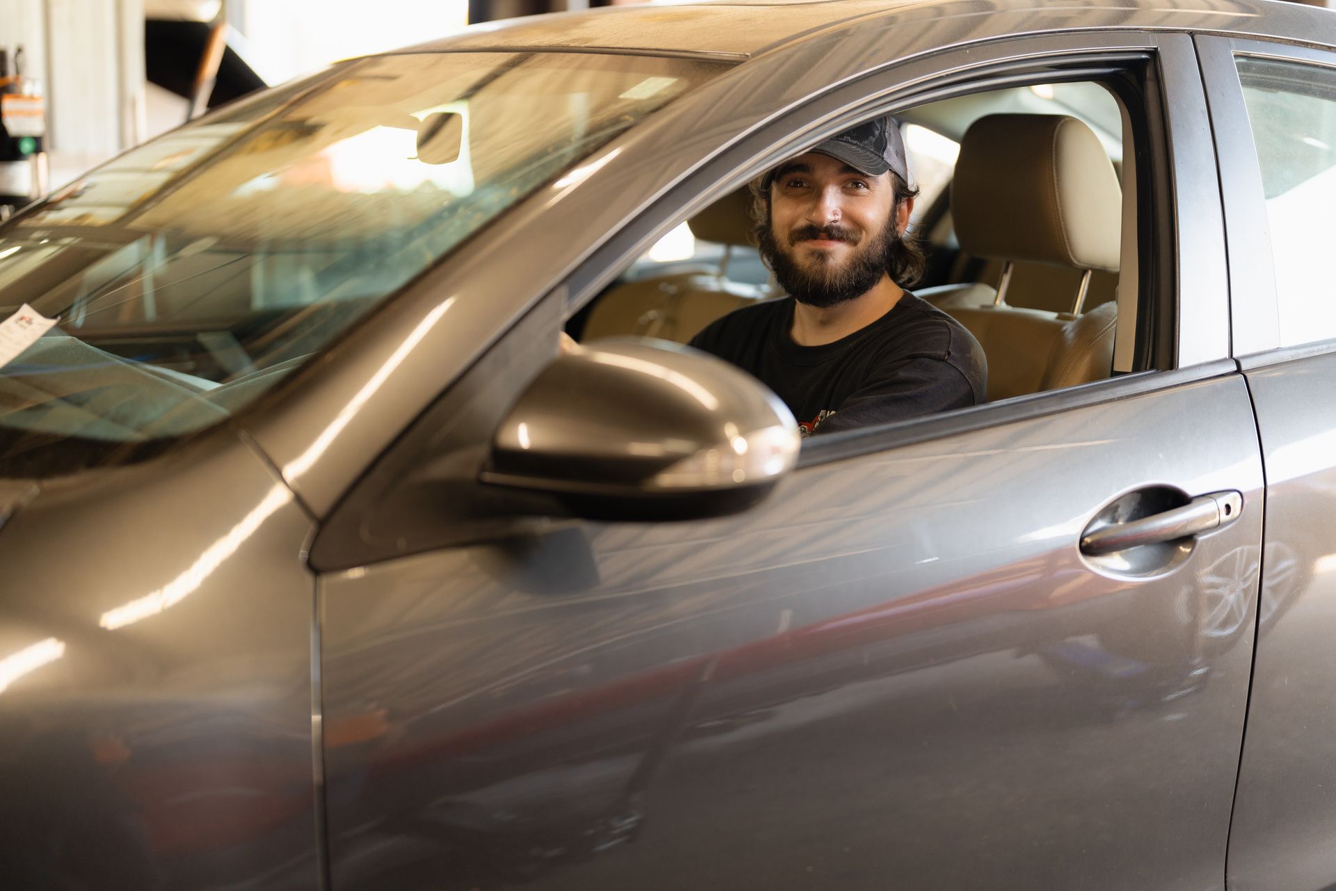 Man smiling from the driver’s seat of a gray car in a parking garage