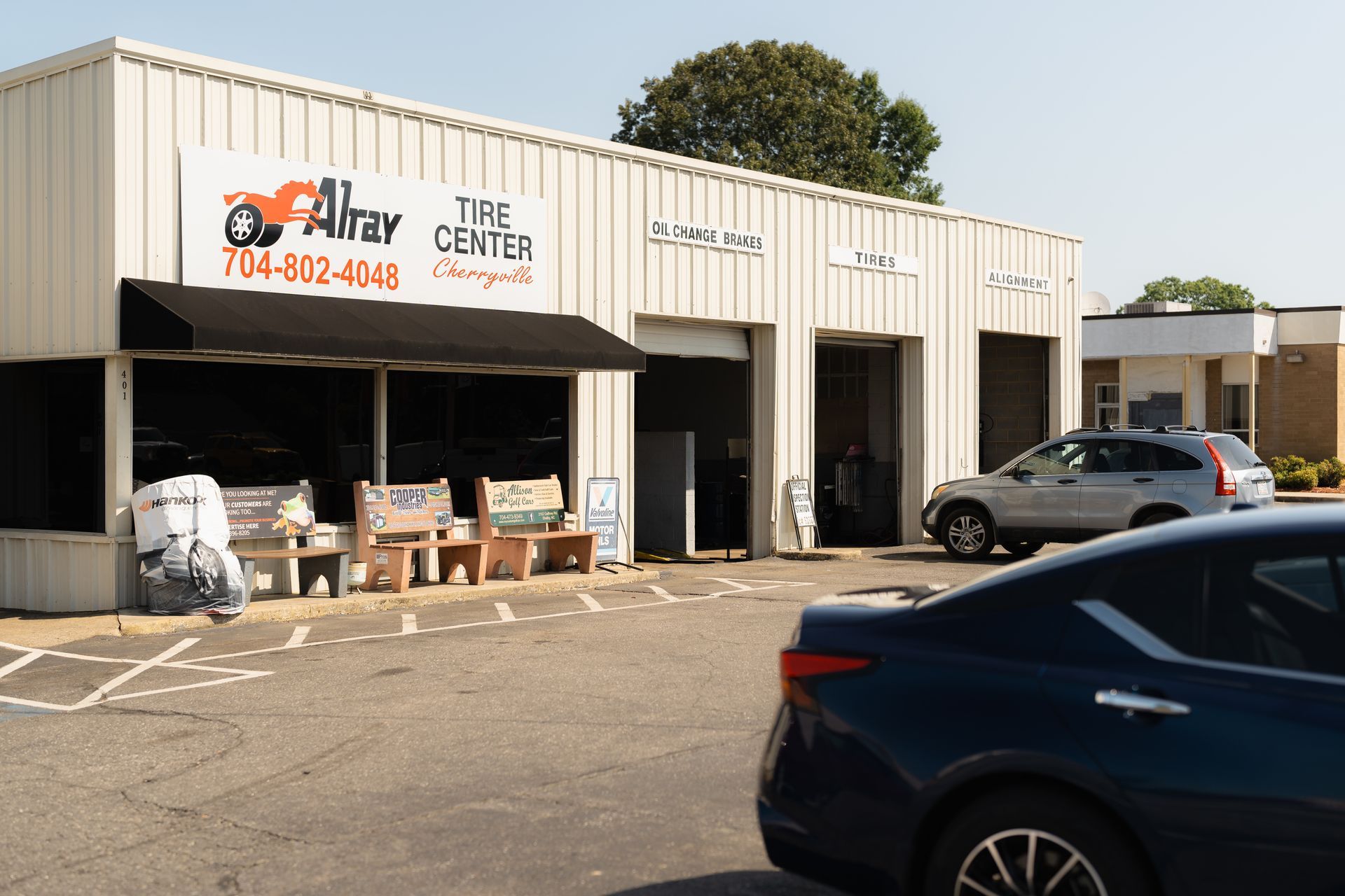 Auto repair shop storefront with open bays, parked cars, and a sign on the building