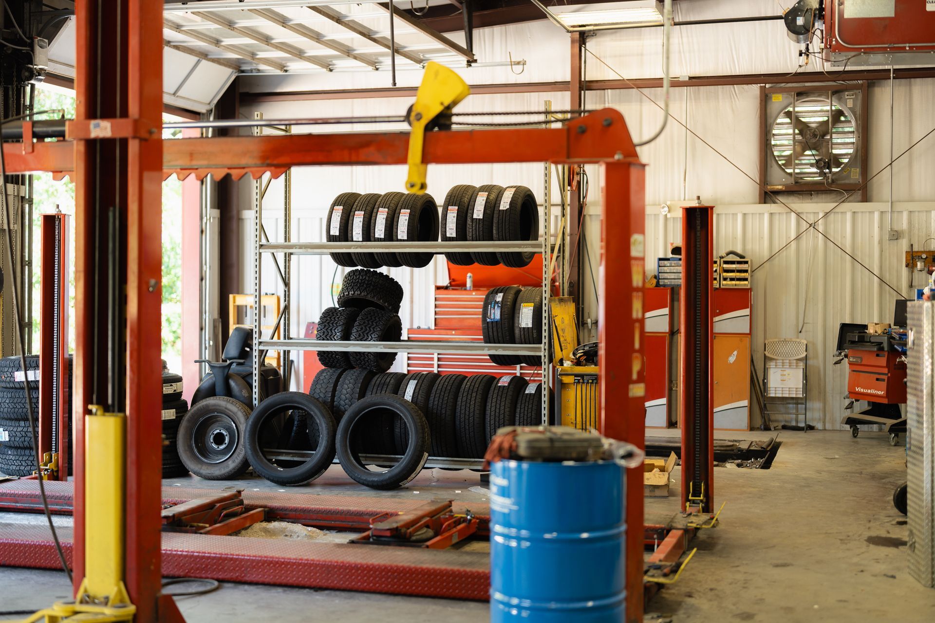 Tire shop with stacks of tires on racks, a yellow forklift overhead, and a blue barrel in the foreground