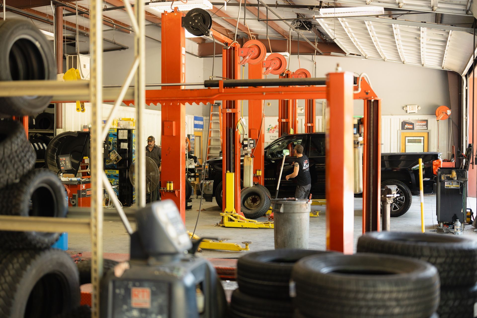 Auto repair shop with orange car lifts, stacked tires, and vehicles in the service bay