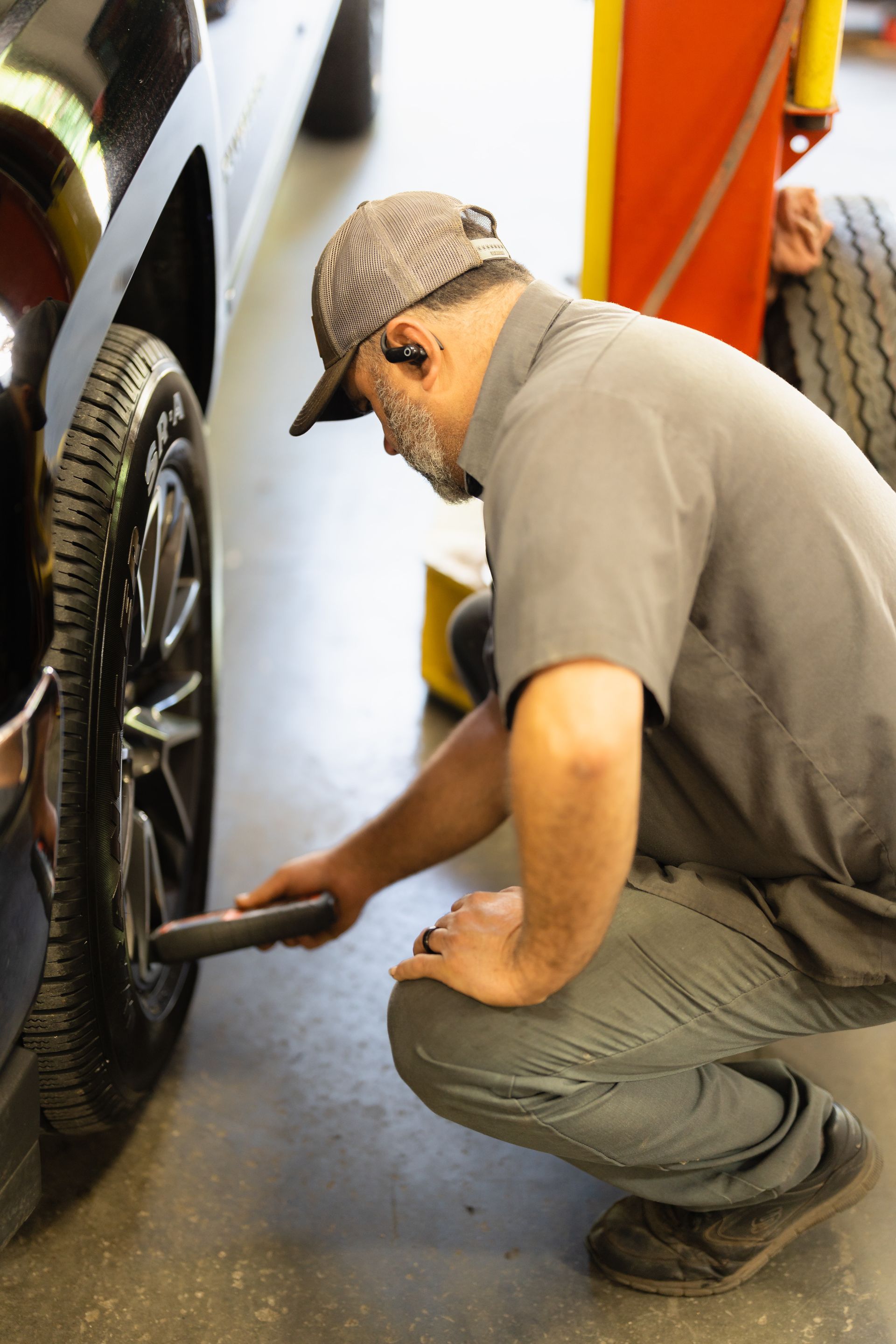 Mechanic crouching beside a truck, checking the wheel with a tool in a garage.