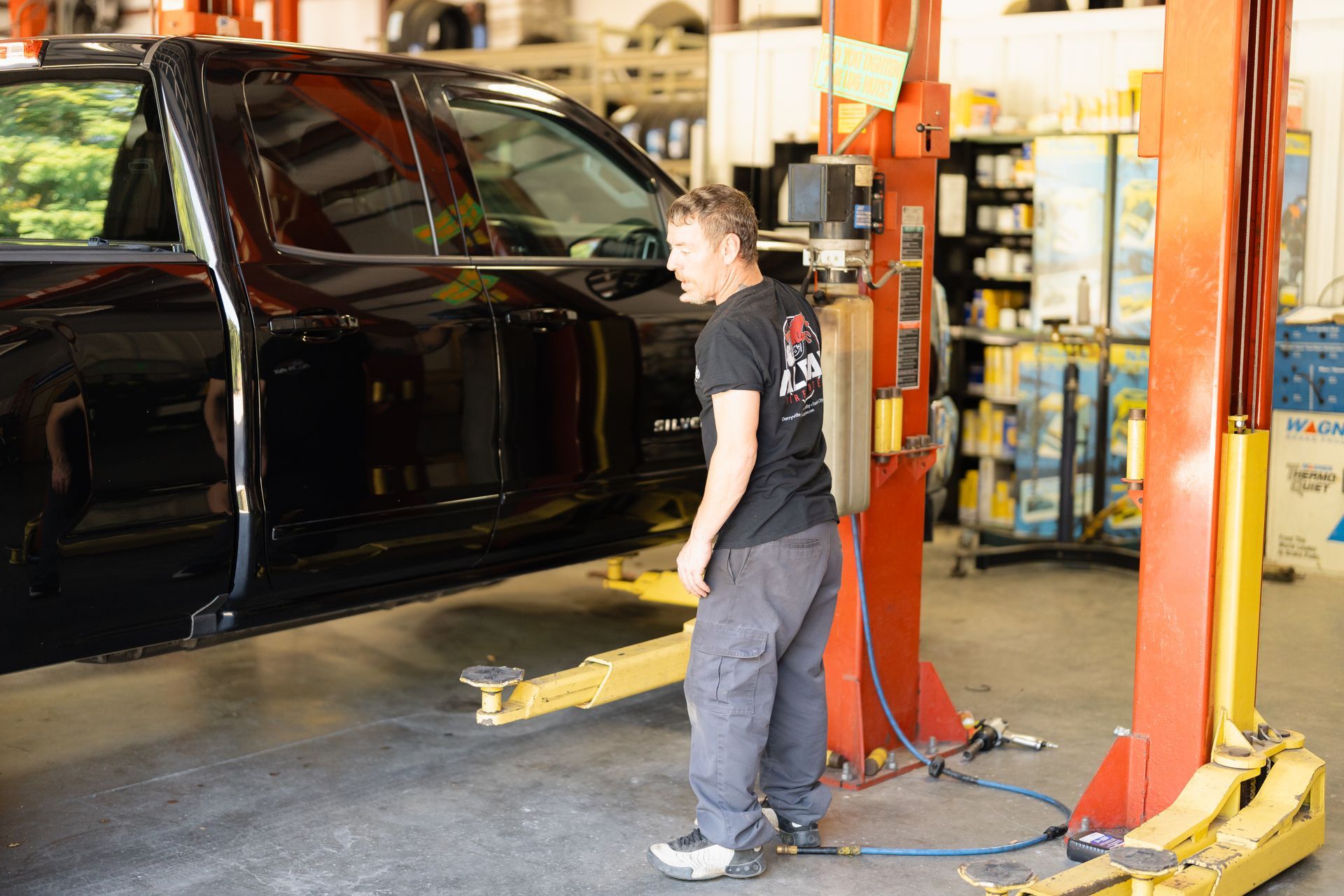 Mechanic standing beside a black van on a vehicle lift in an auto repair shop