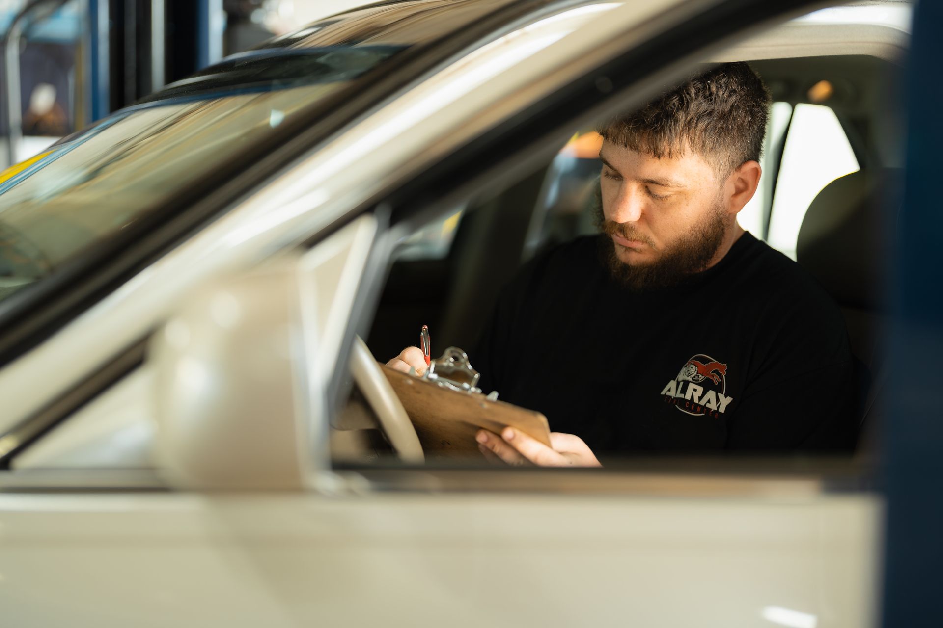 Man writing on a clipboard inside a parked car, seen through the open window.