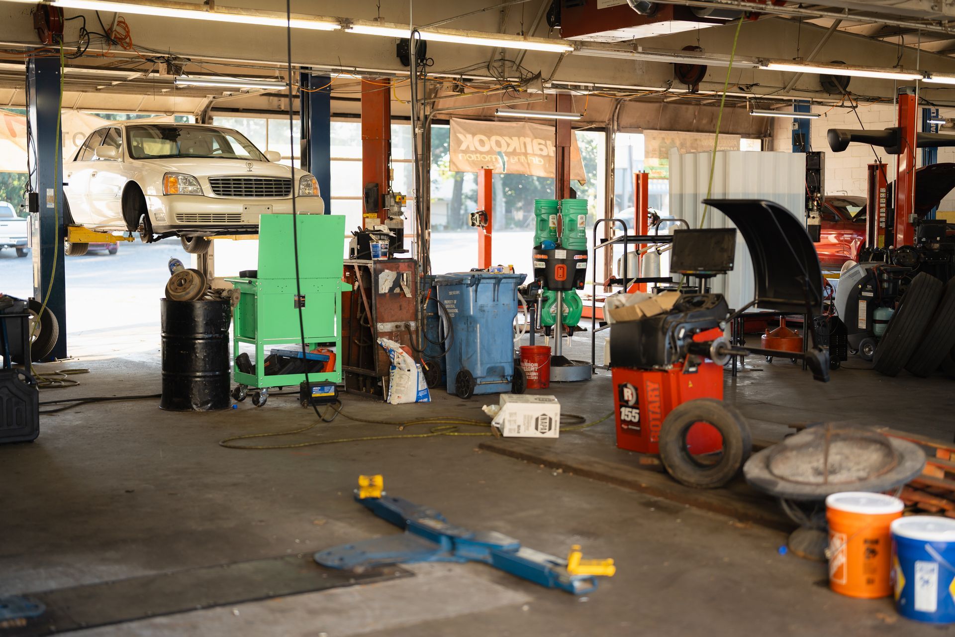 Auto repair shop with cars on lifts, tools, barrels, and shop equipment scattered around.