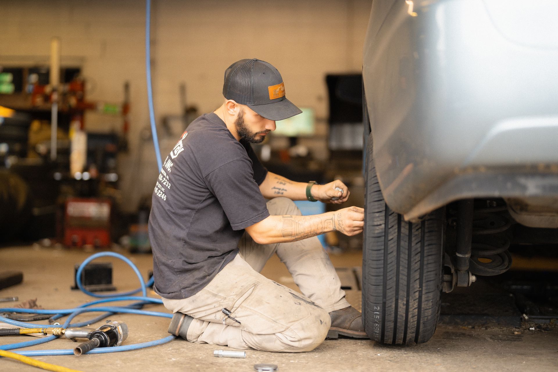 Mechanic kneeling beside a car, working on the front wheel in an auto shop.
