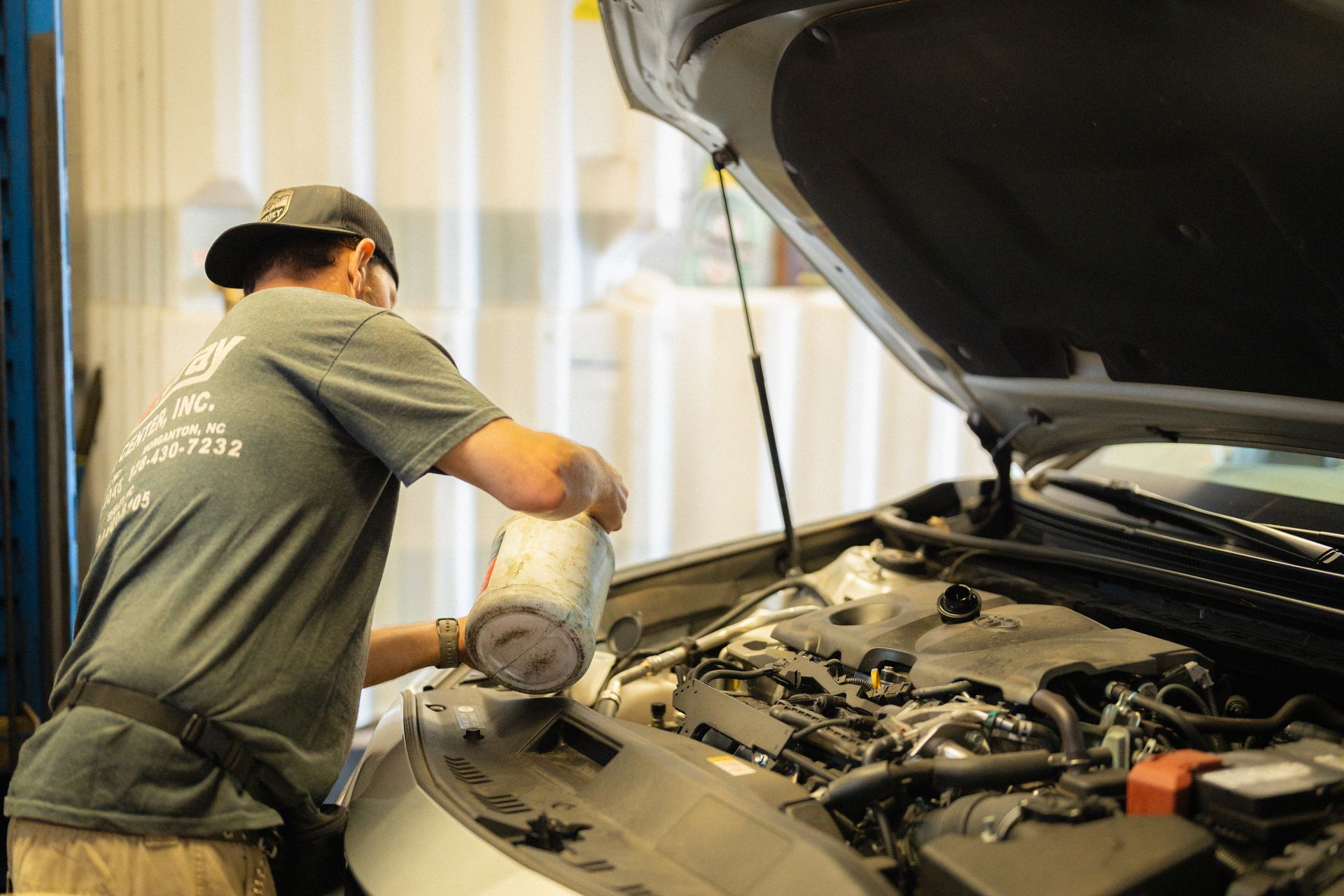 Mechanic using a power tool to work under a car hood in an auto repair shop